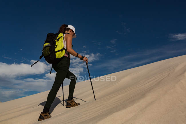 Female hiker with trekking pole walking on sand in desert — Stock Photo