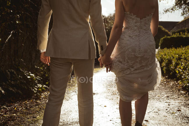 Rear view of bride and groom walking hand in hand in the garden — Stock Photo