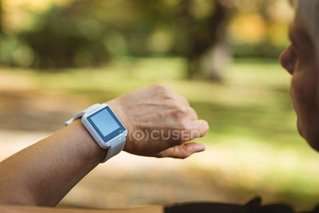 Close-up de mulher idosa usando um relógio inteligente em um parque em um dia ensolarado — Fotografia de Stock