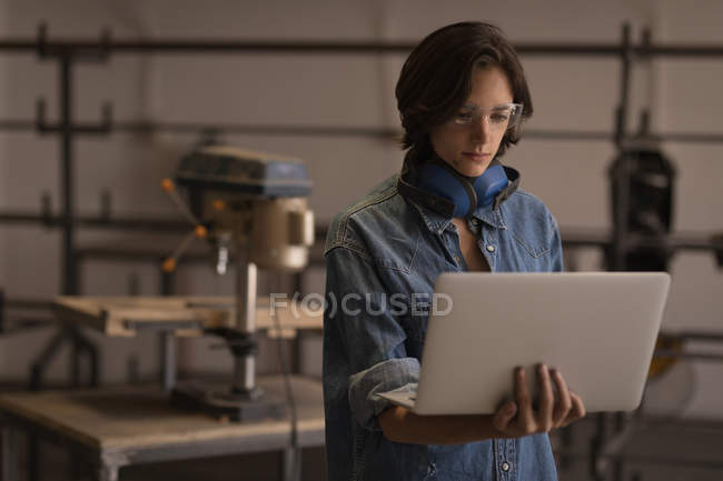 Junge Kunsthandwerkerin nutzt Laptop in Werkstatt. — Stockfoto