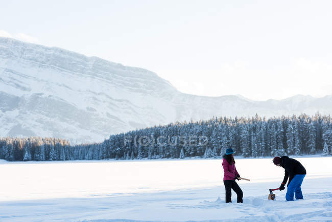 Couple coupe du bois avec hache dans un paysage enneigé en hiver . — Photo de stock