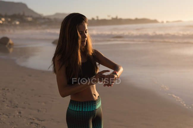 Mulher ajuste usando smartwatch na praia ao entardecer . — Fotografia de Stock