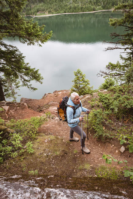 Ältere Frau mit Wanderstöcken im Wald unterwegs — Stockfoto