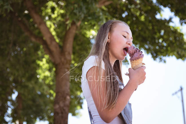 Close-up de menina comendo sorvete sob dossel de árvore . — Fotografia de Stock