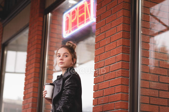 Задумчивая девушка стоит с одноразовым стеклом возле торгового центра — стоковое фото