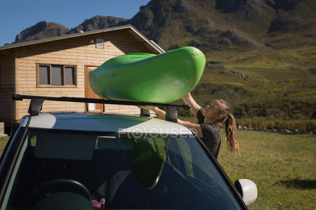 Mulher removendo barco de caiaque de carro por cabana de montanha . — Fotografia de Stock