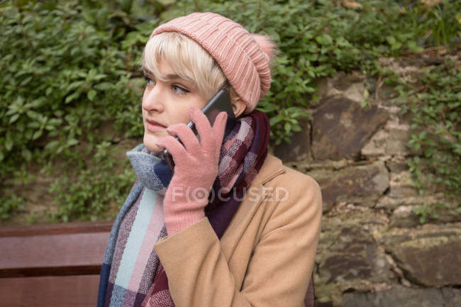 Primer plano de la joven hablando por teléfono mientras está sentada en el banco en el parque - foto de stock