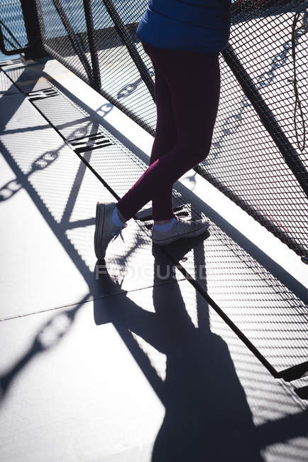 Sección baja de la mujer de pie en el puente durante el día soleado - foto de stock