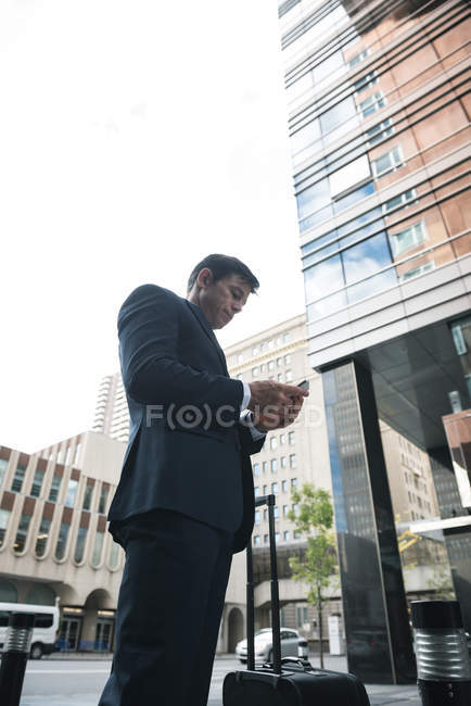 Вид збоку бізнесмена, що використовує мобільний телефон проти хмарочоса — стокове фото