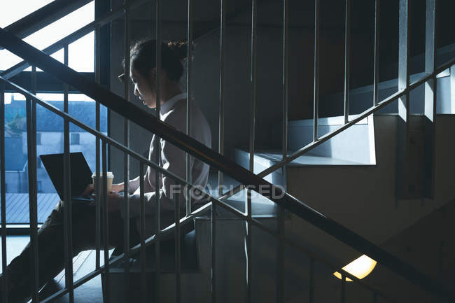 Esecutivo femminile che utilizza laptop sulle scale in ufficio — Foto stock