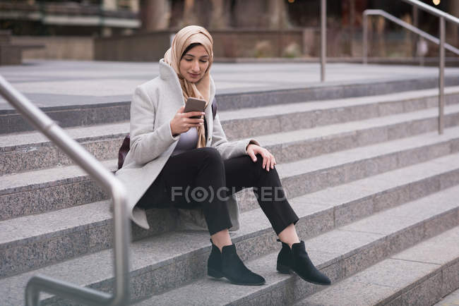 Femme dans le hijab en utilisant un téléphone mobile sur les escaliers — Photo de stock