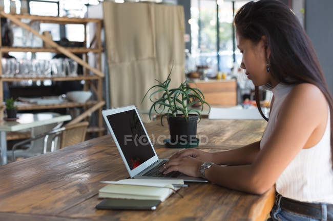 Chica adolescente atenta usando el ordenador portátil en el restaurante - foto de stock