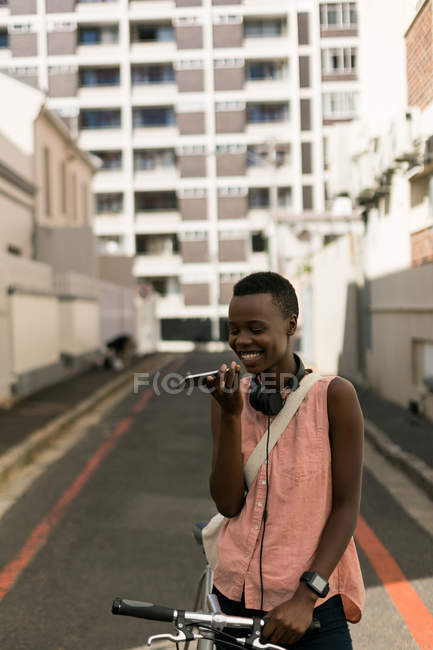 Woman with bicycle talking on mobile phone in city street — Stock Photo