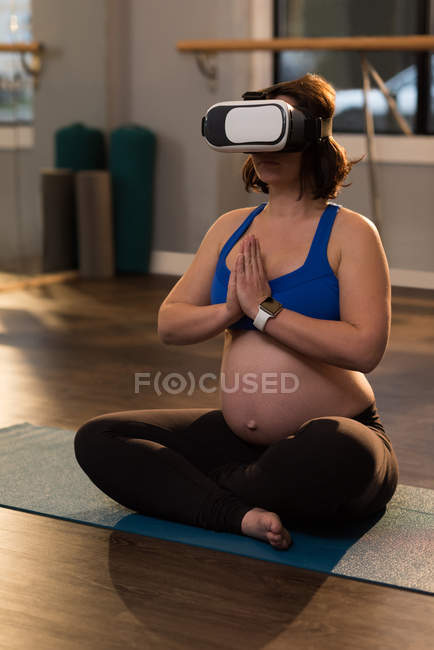 Беременная женщина, занимающаяся йогой, используя виртуальные наушники дома — стоковое фото