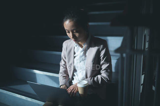 Femme exécutive utilisant un ordinateur portable dans les escaliers du bureau — Photo de stock