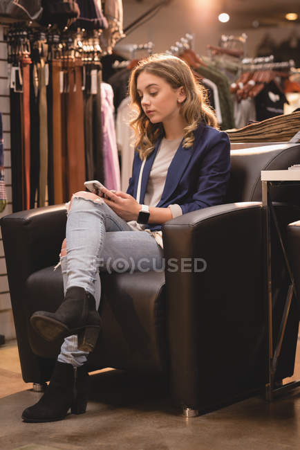 Belle fille utilisant un téléphone mobile sur le canapé au centre commercial — Photo de stock