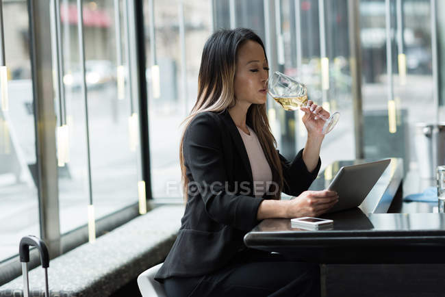 Empresária tomando champanhe enquanto trabalhava em tablet no refeitório — Fotografia de Stock