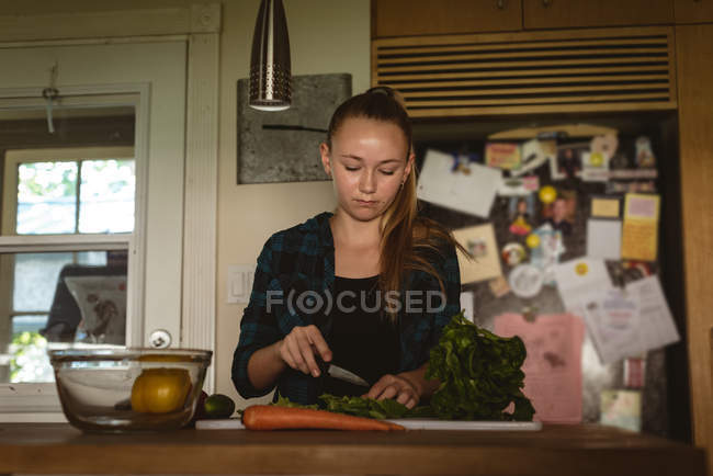 Fille debout dans la cuisine et couper des légumes avec un couteau à la maison . — Photo de stock