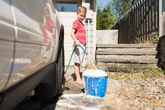 Мальчик заливает воду в ведро во время мытья машины — стоковое фото