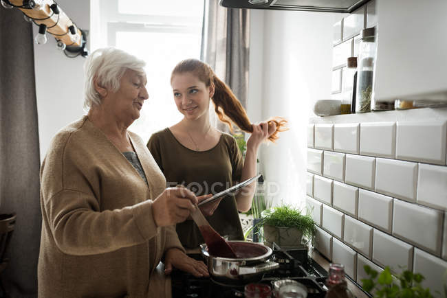 Grandmother and granddaughter cooking raspberry jam in kitchen at home — Stock Photo