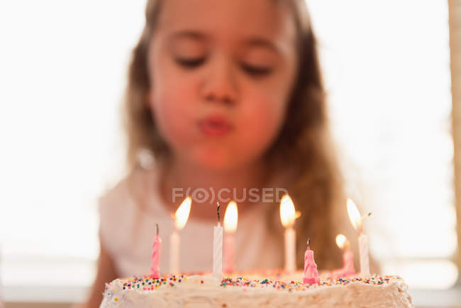 Niña soplando las velas en su pastel de cumpleaños en casa - foto de stock