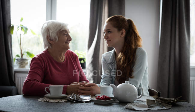 Souriant grand-mère et petite-fille se regardant tout en étant assis dans le salon — Photo de stock