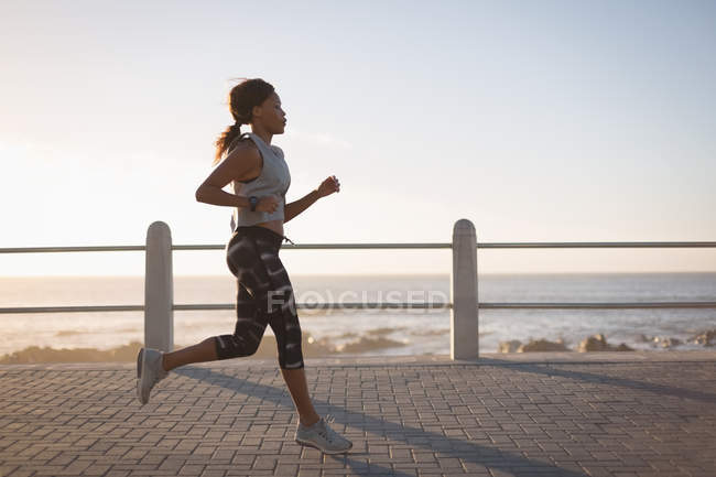 Mujer joven corriendo cerca de la playa al atardecer - foto de stock