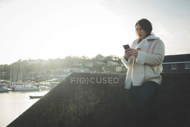 Femme utilisant un téléphone portable près de la rivière au soleil . — Photo de stock