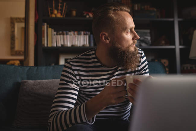 Thoughtful man looking away while having coffee at home — Stock Photo