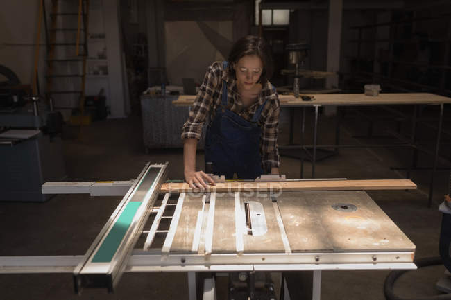 Jeune artisan femelle mesurant une pièce en bois en atelier . — Photo de stock