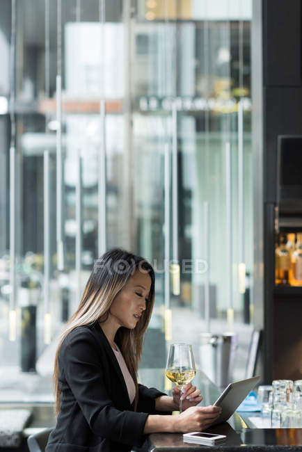 Mujer de negocios con el pelo de color que tiene champán mientras usa la tableta en la cafetería - foto de stock