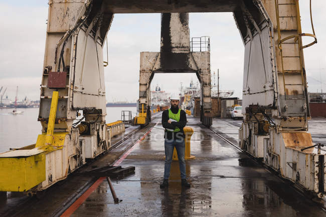 Retrato del trabajador portuario de pie con los brazos cruzados en el astillero - foto de stock
