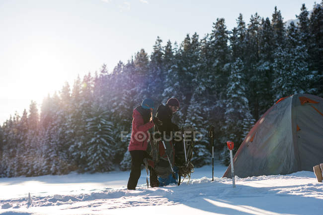 Caminhada de casal com mochilas para tenda juntos na floresta nevada . — Fotografia de Stock