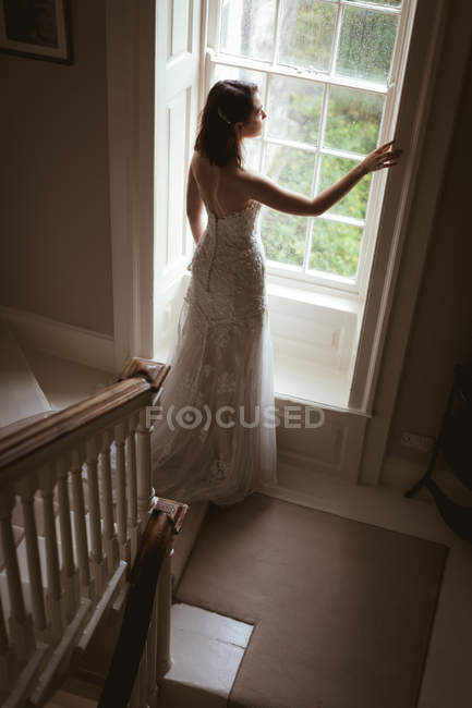 Rückansicht der Braut, die zu Hause aus dem Fenster schaut — Stockfoto