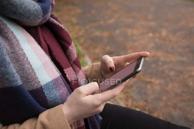 Крупный план средней части молодой женщины, использующей мобильный телефон в парке — стоковое фото
