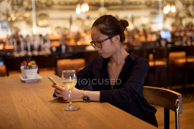 Mujer usando el teléfono móvil mientras toma vino en el hotel - foto de stock