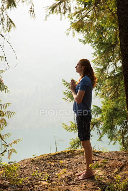 Fit man standing in meditating posture on the edge of a rock at the time of dawn — Stock Photo