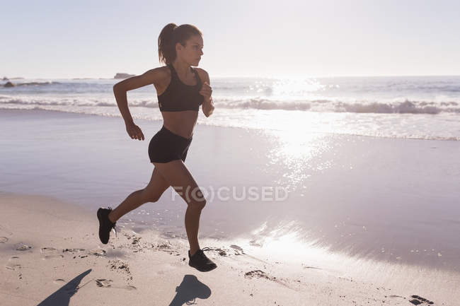 Fitte Frau joggt in der Abenddämmerung am Strand. — Stockfoto