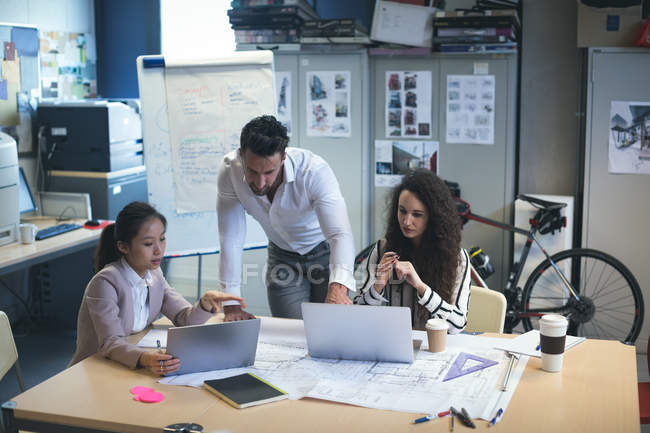 Ejecutivos discutiendo sobre el ordenador portátil en la oficina moderna - foto de stock