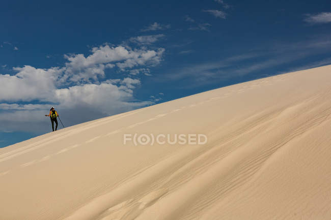 Hiker with trekking pole walking on sand on a sunny day — Stock Photo
