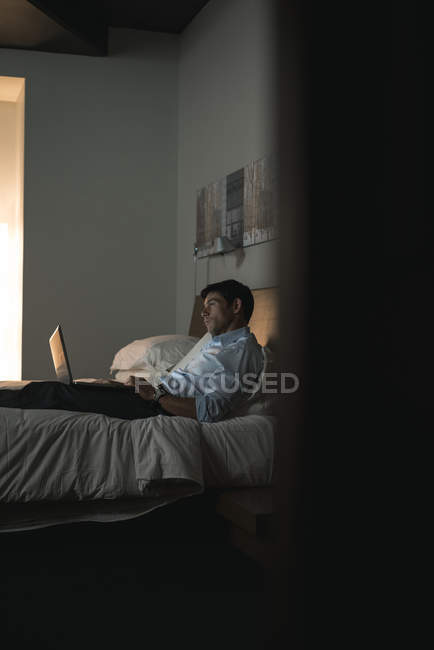 Homme d'affaires utilisant un ordinateur portable dans la chambre à coucher à l'hôtel — Photo de stock