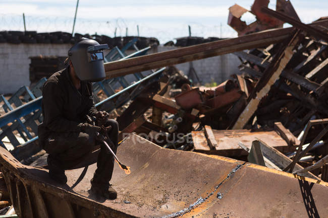 Trabajador cortando el metal en el desguace en un día soleado - foto de stock