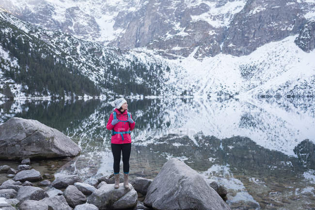 Женщина с рюкзаком стоит на берегу озера зимой — стоковое фото