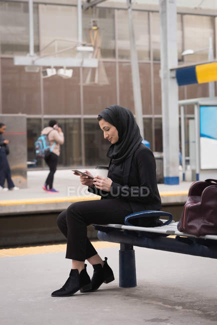 Femme en hijab utilisant un téléphone portable à la gare — Photo de stock