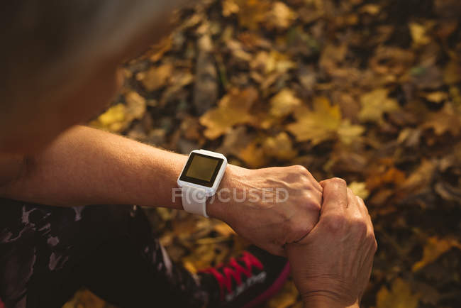 Femme âgée utilisant une montre intelligente dans un parc à l'aube — Photo de stock