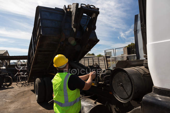 Vista trasera del trabajador levantando el contenedor de un camión volquete - foto de stock