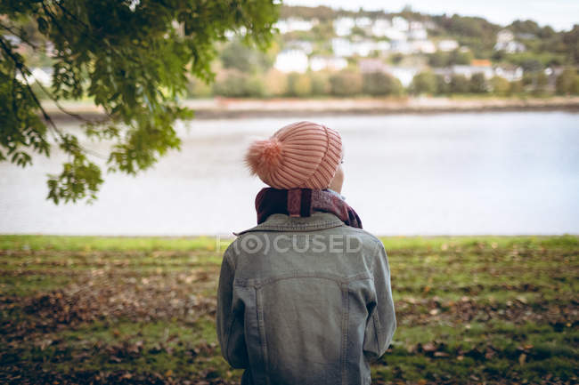 Rear view of young woman wearing warm clothing standing near river coast — Stock Photo