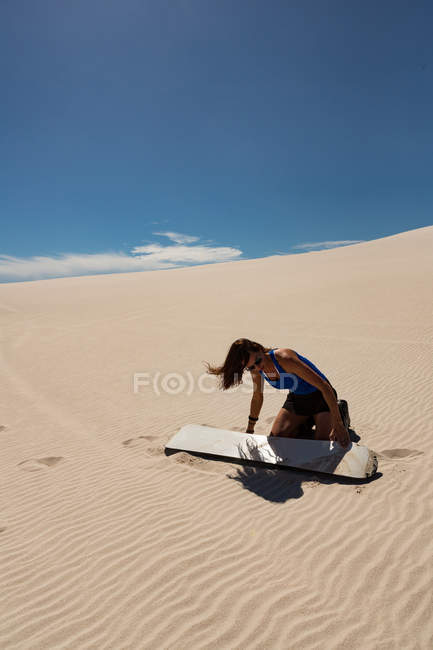 Femme appliquant de la cire de planche de surf sur un plateau de sable au désert par une journée ensoleillée — Photo de stock