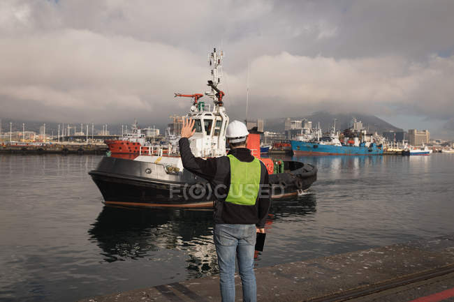 Dock worker waving hand to sailing boat in port — Stock Photo