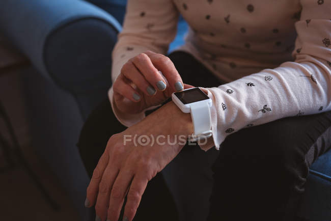Close-up of woman using a smart watch while sitting on sofa in living room — Stock Photo